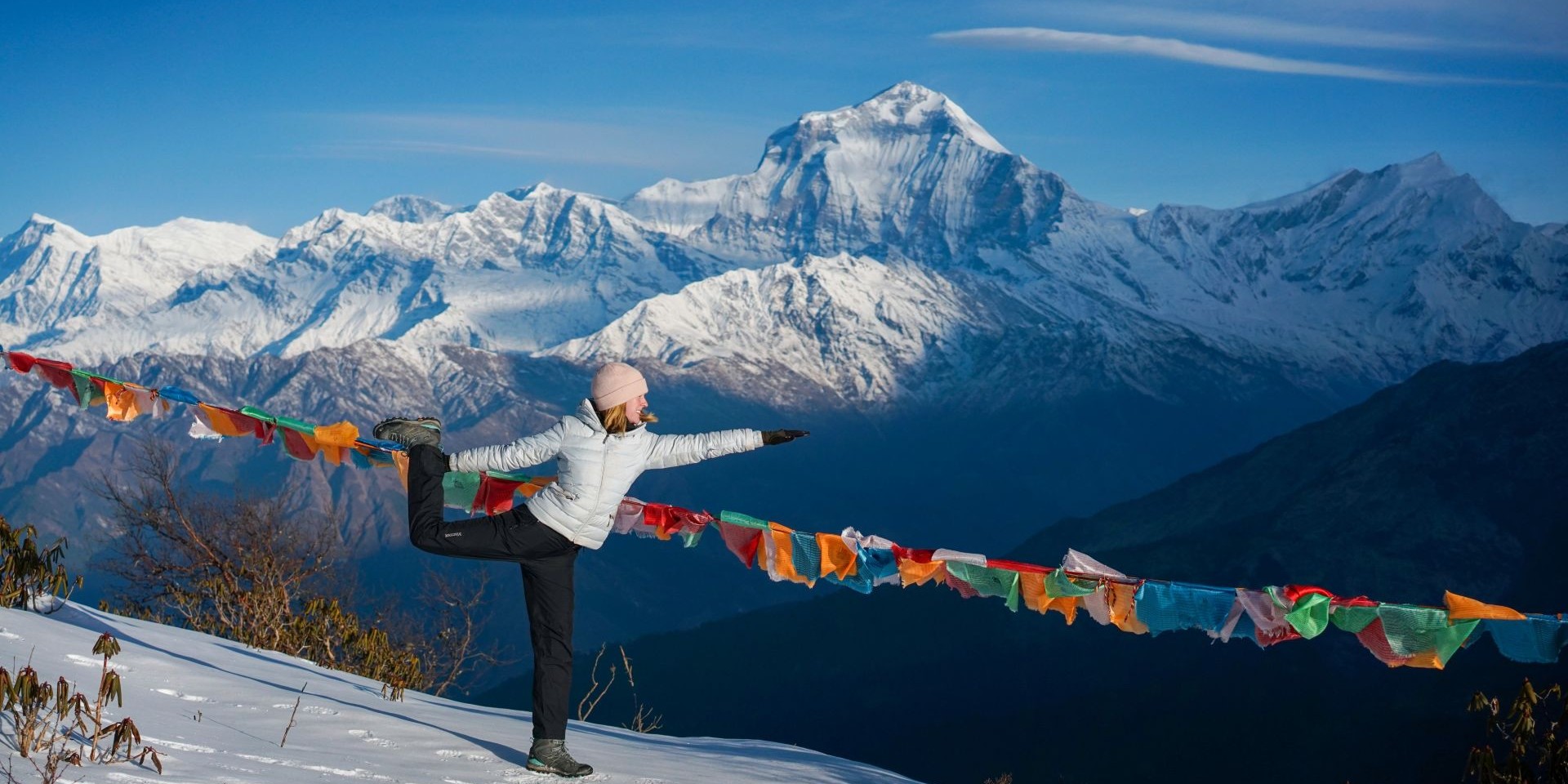 Woman wearing trekking gear, doing a yoga pose in front of prayer flags and Himalayan mountain views
